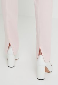 Light pink tailored trousers with split hems, paired with white high-heel shoes featuring a chunky heel and rounded toe design.