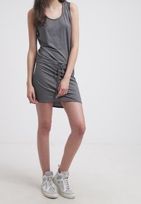 Szara sukienka bez rękawów z marszczonym bokiem, szczegółem z sznurkiem i miękką fakturą. Połączona z białymi sneakersami za kostkę z szarymi akcentami.