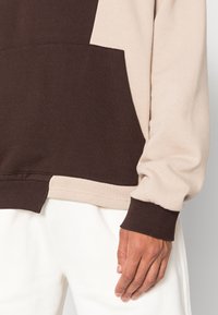 Felpa girocollo con un design a blocchi di colore in beige chiaro e marrone scuro, dotata di tasca frontale e polsini a costine.