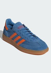 Blue suede sneaker with mesh panels, orange stripes, and rubber sole. Features textured surface and flat laces for secure fit.