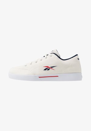 Zapatilla de lona blanca con acentos en azul y rojo, que presenta seis ojetes, cordones planos, una suela acolchada y un logo en el costado.