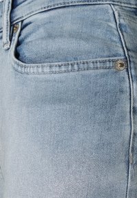 Jeans de mezclilla azul claro que presentan un bolsillo frontal y un cierre de botón metálico, mostrando una textura suave con sutiles detalles de costura.