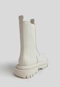 Chunky white ankle boots with a smooth synthetic upper, elastic side panels, and a textured rubber sole with deep treads.