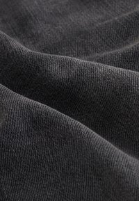 Close-up of soft, dark gray fabric with fine knit texture and gentle folds creating light and shadow variations.