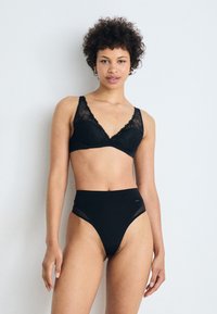 Zwarte kanten beha met een driehoekige vorm en golvende randen, gecombineerd met high-waisted zwarte slipjes met gaasdetails en minimale branding.