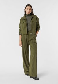 Krótkia kurtka w oliwkowej zieleni z dużymi przednimi kieszeniami, zestawiona z szerokimi spodniami w tym samym kolorze. Pod spodem prążkowany golf o fakturze. Czarne buty na platformie.