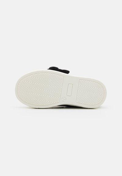 Scarpa nera con tomaia strutturata e suola in gomma bianca. Presenta un motivo a zigzag sulla suola e una morbida fascia in tessuto per la chiusura.
