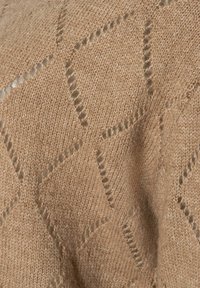 Beige gestrickter Stoff mit einem Rautenmuster, das offene Maschen aufweist und eine weiche Textur hat. Das Material wirkt warm und atmungsaktiv.