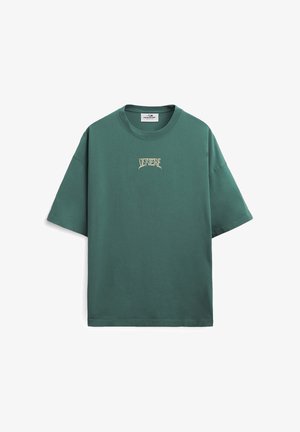 Zielony, oversize'owy t-shirt z krótkim rękawem, okrągłym dekoltem i stylizowanym beżowym logo z tekstem na środku klatki piersiowej.