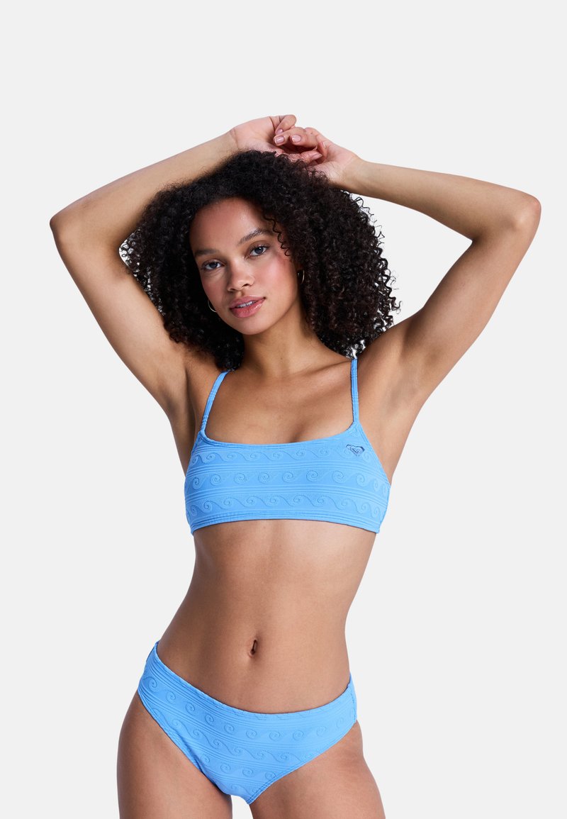Σετ μπικίνι γαλάζιου χρώματος με τοπ cropped και αντίστοιχα σλιπ. Υφασμάτινη υφή με κυματιστό μοτίβο. Λεπτές τιράντες και χαμηλή μέση.