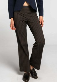 Pantalons rayés bruns avec une taille haute, fabriqués à partir d'un tissu texturé. Les pantalons sont à jambes larges avec une coupe décontractée, complétés par des mocassins noirs.