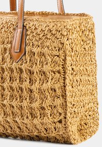 Wykonana z plecionej słomy torebka w naturalnym odcieniu brązu, o prostokątnym kształcie, mocnych skórzanych uchwytach i teksturowanym, otwartym splotem.