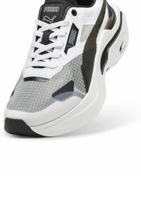 Sneaker Puma con tomaia in rete grigia traspirante, suola bianca, dettagli neri e lacci spessi. Motivo a griglia distintivo sul materiale.