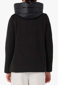 Giacca nera con una finitura testurizzata, dotata di un cappuccio nero gonfio, silhouette dritta e design minimalista.