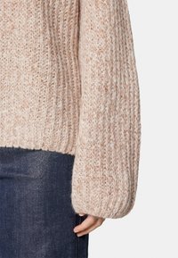 Světle růžový pletený svetr s ribbovanou texturou a širokými, oversized rukávy. Lem je mírně zkrácený, spárován s tmavými džíny.