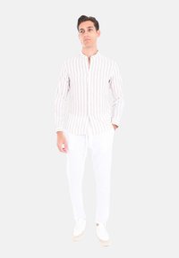 Camicia a maniche lunghe a righe in morbido tessuto, con righe bianche e beige chiaro, colletto alla mandarina; abbinata a pantaloni bianchi e sneaker chiare.