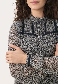 Genomskinlig blommönstrad blus i marinblått och krämfärgat med en volangkrage, svart spetsdetalj, knappstängning och samlade manschetter.