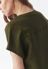 Olivegrüne Bluse mit kurzen Ärmeln aus leichtem Stoff, mit einer Nahtdetail über den Rücken und einer lockeren Passform.