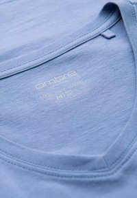 Světle modré bavlněné tričko s v-výstřihem. Má štítek s nápisem "Ombre, 100% čistá bavlna, M." Hladká textura, jednoduché detaily.