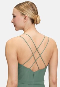 Zielona sukienka z krzyżującymi się ramiączkami na plecach, o gładkim wykończeniu i ukrytym zapięciem na zamek w talii.