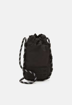 Sac à cordon noir en tissu durable, avec un patch logo texturé et des bretelles à motif noir et blanc. Forme cylindrique compacte.