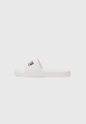 Valged libisemisjalanõud, millel on üks rihm musta logoga, tasane tall, sile tekstuur ja ümarad servad. Minimalistlik disain.