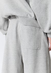 Grå joggingbukser lavet af blødt stof med elastisk taljebånd og en stor, rektangulær lomme på højre baglomme. Tekstureret finish synlig.