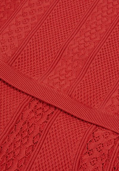 Tissu tricoté d'un rouge vibrant avec un motif texturé comprenant des designs entrelacés et des accents côtelés, créant un effet visuel en couches.