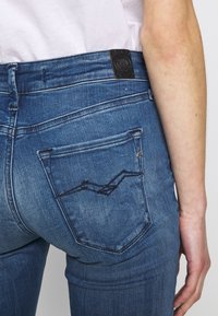 Vaqueros de mezclilla para hombre, color azul medio, con un bolsillo trasero con costuras en contraste, ajuste estrecho y una etiqueta en la cinturilla texturizada.