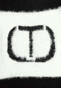 Gros plan sur un tissu en maille pelucheux noir et blanc avec un motif audacieux et stylisé "CD" en couleurs contrastantes.