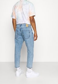 Jasnozmywane dżinsy o luźnym kroju, z prążkowanym paskiem i dwoma tylnymi kieszeniami. W połączeniu z pastelowym tie-dye t-shirtem i białymi trampkami.