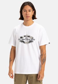 Camiseta de algodón blanca con un diseño gráfico en negro y verde con el texto "Quiksilver" en el centro, de manga corta y cuello redondo.