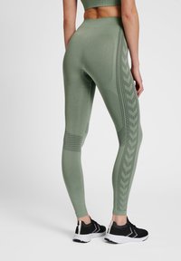 Leggings verts ajustés en tissu extensible, avec un motif texturé sur les côtés et une taille haute.