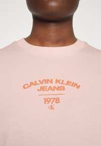 Růžové bavlněné tričko s kulatým výstřihem a obrovským oranžovým logem: "CALVIN KLEIN JEANS 1978" a akcentem "ck".