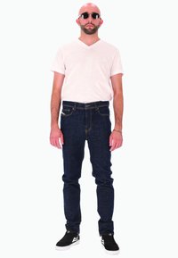 T-shirt blanc à col en V, jean bleu foncé avec coutures orange, baskets noires et lunettes de soleil rondes. Coupe droite et style décontracté.