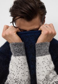 Sweter dzianinowy z granatowym tułowiem, szarymi i białymi nakrapianymi rękawami. Miękka tekstura, ściągacze na mankietach i wysoki kołnierz.