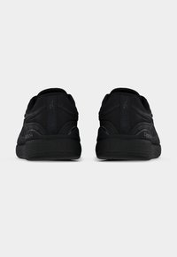 Ζευγάρι μαύρα αθλητικά παπούτσια Reebok, εμφανιζόμενα από πίσω, με έμφαση στις υφασμένες σόλες και τις ετικέτες με το λογότυπο στη φτέρνα, σε απλό φόντο.