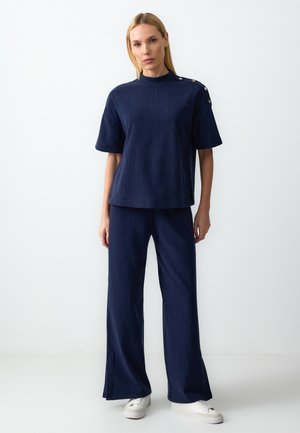 Navyblauwe textuur korte mouw top en wijde broek set. Heeft knoopdetails op de schouder. Gecombineerd met witte platform sneakers.