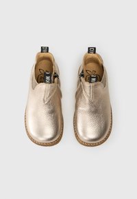 Chaussures en cuir doré métallisé pour tout-petits avec des bouts ronds, fermeture éclair sur le côté, poignées noires et semelles brunies sur un fond blanc.