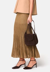 Sac en suède brun avec un rabat et une courte anse, associé à une jupe plissée dorée métallique et des escarpins en vernis noir avec des brides au niveau de la cheville.