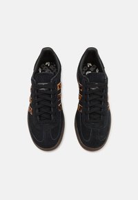 Baskets en daim noir avec des accents de léopard brun, présentant un design classique à lacets et une semelle en caoutchouc texturée.