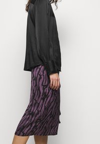 Blusa de satén negro de manga larga con puños abotonados, combinada con una falda de longitud media morada que presenta un estampado de animales en negro.