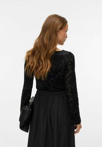 Melnā garām piedurknēm tops ar ziedu mežģīņu rakstu, apvienots ar melnu svārku. Topam ir apaļa kakla izgriezums un caurspīdīgas piedurknes.