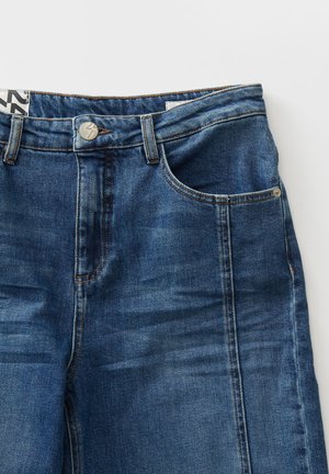 Jeans aus Denim in mittlerem Blau mit glatter Oberfläche, Fünf-Taschen-Design, knopflosem Verschluss vorne und Kontrastnähten.