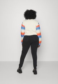 Suéter blanco de punto trenzado con mangas en degradado rojo y azul, combinado con jeans skinny negros y zapatos de plataforma negros.