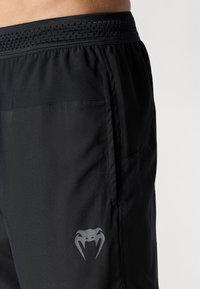 Shorts de sport noirs avec une taille côtelée, des poches sur les côtés et un logo gris avec un design de serpent sur le bas à l'avant.