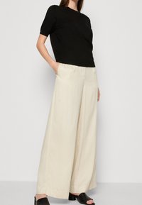 Černé tričko s krátkým rukávem v kombinaci s krémovými kalhotami do široka. Oblečení má jednoduchý design a hladké textury. Černé sandály s otevřenou špičkou.