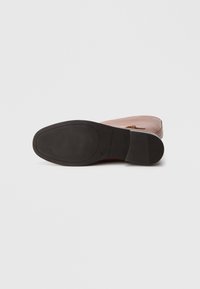 Bottine en cuir marron avec une semelle en caoutchouc noire plate, présentant une texture subtile et une bride décorative autour de la cheville.