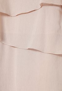 Vaaleanpunainen kangas, jossa on teksturoitu pinta ja kerroksittain asetellut röyhelöt yläreunassa. Sileä pinta, jossa on hienovarainen kiilto.