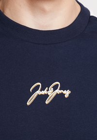 Felpa blu navy con collo rotondo, con il logo cursivo bianco e arancione "Jack & Jones" centrato sul petto.